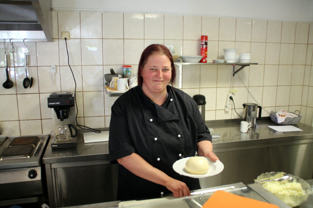 Frau Seidel freut sich,dass sie als Köchin bei einem Partyservice arbeien kann. Mit Freude verteilt sie auf dem Foto Hefeklöse auf Teller. 